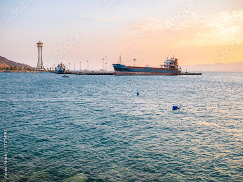 Scenic view at sunset with a docked old rusted ship and the lighthouse observation tower in the port of Aqaba city, Jordan. photo