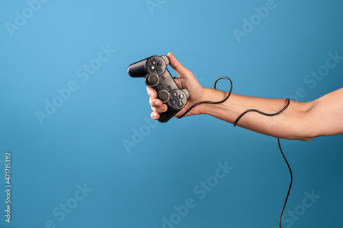 Play computer games ,become a professional gamer. A man's hand holds a gamepad with a wire, a photo on a blue background photo