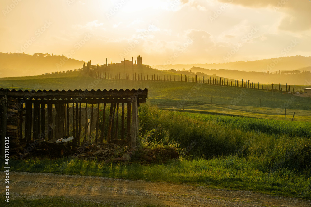 Tuscany, italy, may 2018, a farm on a hilltop against an orange sunset sky, a barn in the foreground
