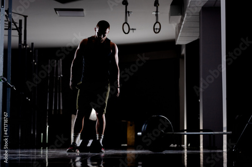 Silhouette of a muscular athlete with weights. Standing next to heavy barbell