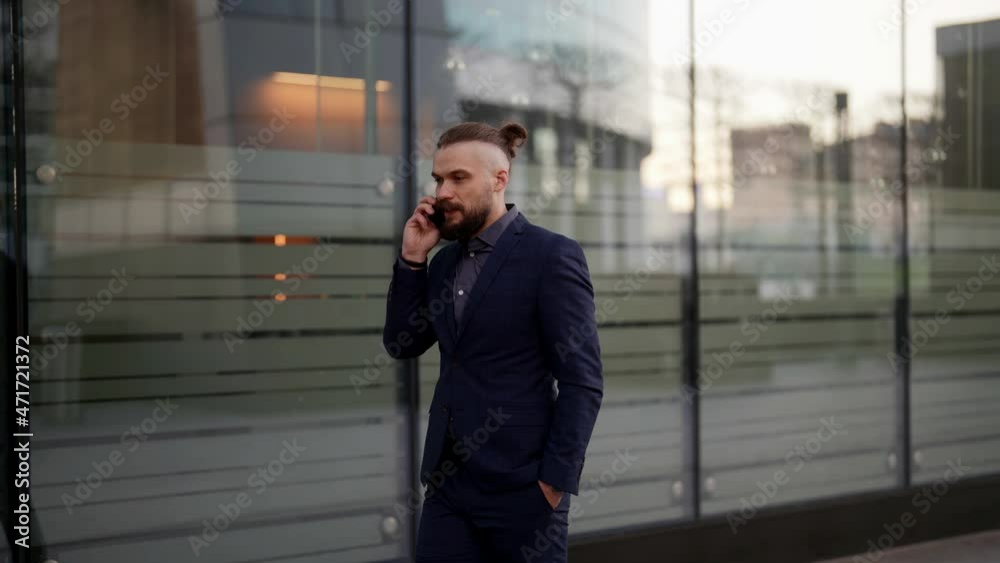 bearded young man dressed in business suit is calling by cellphone and walking on city street bearded young man dressed in business suit is calling by cellphone and walking on city street