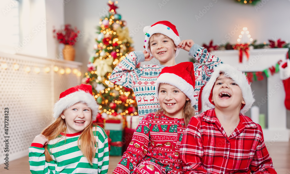 Happy children sitting in the living room at home in christmas pajamas Happy children sitting in the living room at home in christmas pajamas