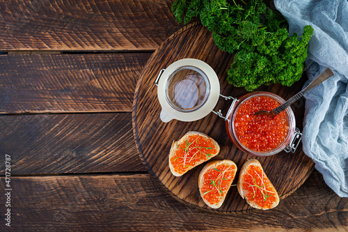 Delicious fresh red caviar with baguette toasts on wooden background. Top view