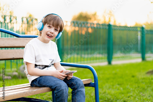 boy on the street sits on a bench with headphones and with a phone