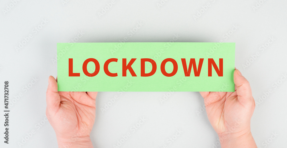 The word lockdown is standing on a green paper, Covid-19 pandemic regulations, hands holding the message The word lockdown is standing on a green paper, Covid-19 pandemic regulations, hands holding the message