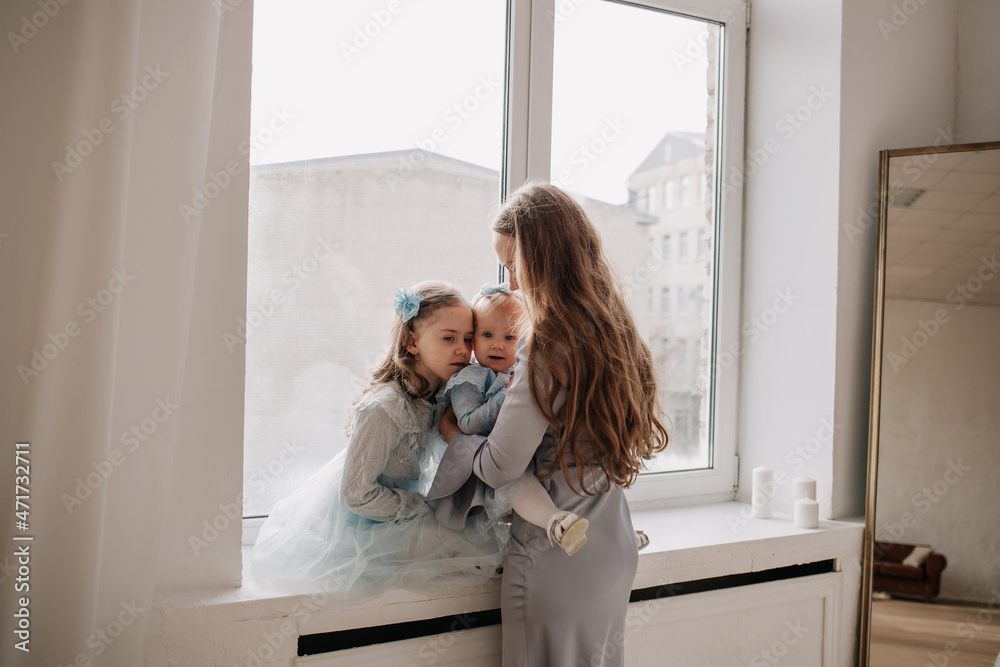 a beautiful mother and her daughters are sitting on the windowsill near the window in a room with a mirror a beautiful mother and her daughters are sitting on the windowsill near the window in a room with a mirror