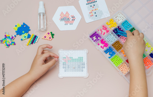 Children's educational game aqua mosaic, a small child inserts multicolored beads into the pattern with a special pen.
