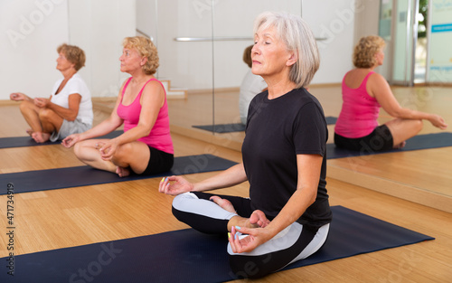 Mature women in sportswear exercising lotus pose together during group yoga class.