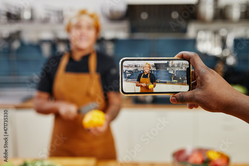 Portrait of smiling female cook on smartphone screen recording videos or livestream in kitchen, copy space photo