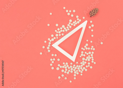 A modern Christmas concept. The simplicity of white and coral color. A white triangle as a Christmas tree. Copy space. Small white balls and a little cone. Asymmetric elements. New Year's event. photo