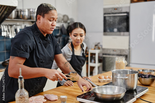 Side view portrait of female chef frying meat during cooking class in kitchen interior