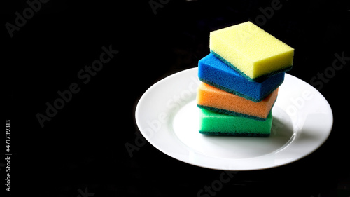 Clean white plate and multi-colored scouring sponges on a black background