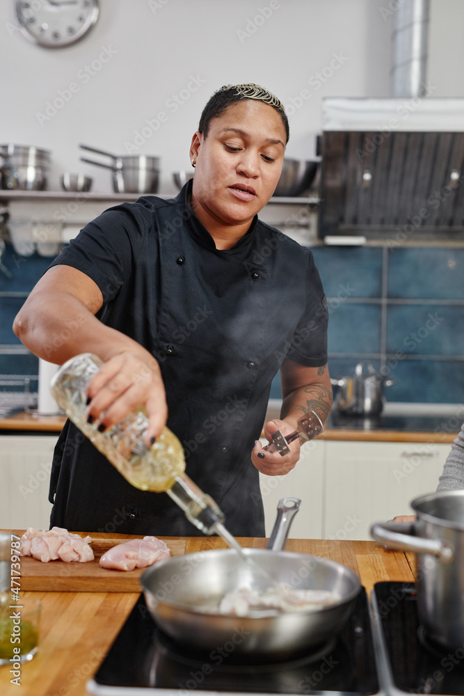 Vertical portrait of tattooed female chef frying meat while cooking in professional kitchen