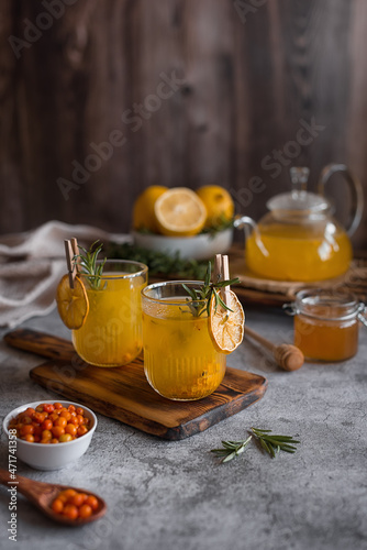 Sea buckthorn tea in a glass teapot and mugs with lemon, honey and ginger. Vertical photo.