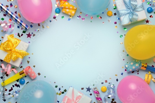 Holiday frame or background with colorful balloon, gift, confetti, silver star, carnival cap and streamer. Birthday or party greeting card with copy space. Flat lay, top view.