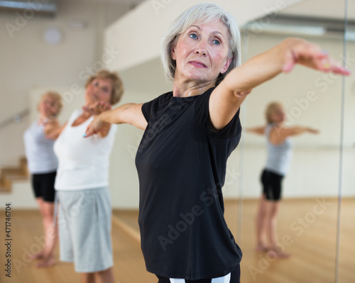 Group of aged women who are engaged in the dance section in the studio are standing in the 2nd position of the ballet stand ..near the mirror