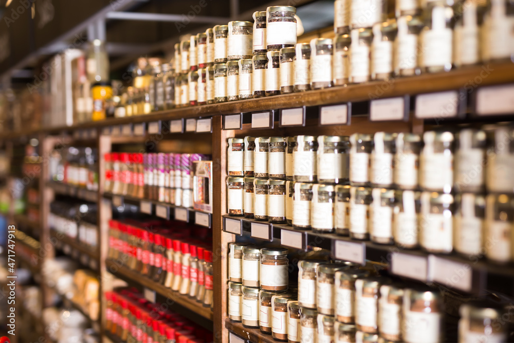 Rows of glass jars with natural spices and herbs lined up on shelves in grocery store
