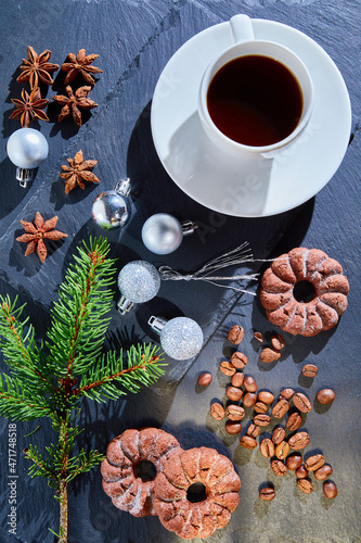 A cup of coffee on a saucer on a stone stand. Cookies, star anise, Christmas balls, coffee beans, a fir branch on a blue background. Top view food