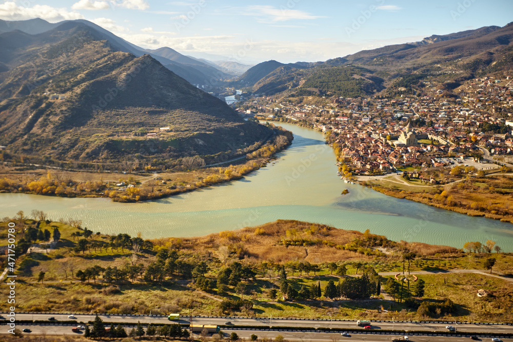 View from afar of the town of Mtskheta, the UNESCO world heritage city and the Mtskheta river in a blur background of mountains and villages in Georgia under blue sky