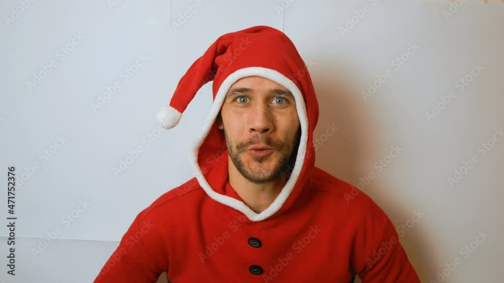 A young funny guy in a New Year's elf costume smiles and waves his hand in greeting. A young handsome guy in a red santaclaus carnival costume shakes his head and smiles broadly. A young funny guy in a New Year's elf costume smiles and waves his hand in greeting. A young handsome guy in a red santaclaus carnival costume shakes his head and smiles broadly.