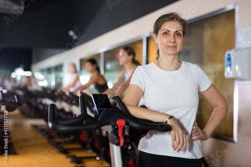 Elderly woman in activewear warming up on bike in spin class at gym