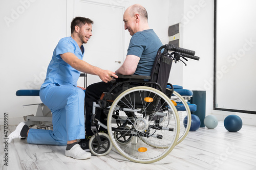 Male Physiotherapist helping a patient with a disability who uses a wheelchair to get up at rehabilitation hospital. High quality photo.