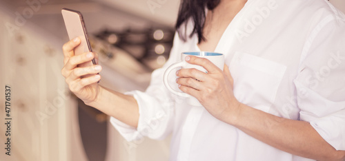 Selective focus to hands of person holds a cup and uses a smartphone.
