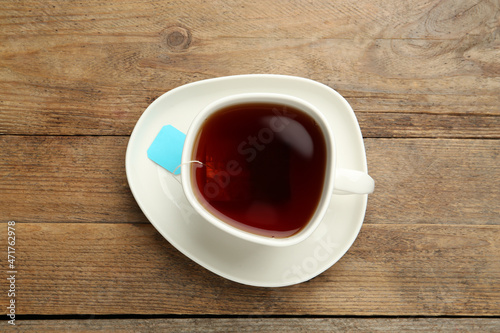 Tea bag in ceramic cup of hot water on wooden table, top view