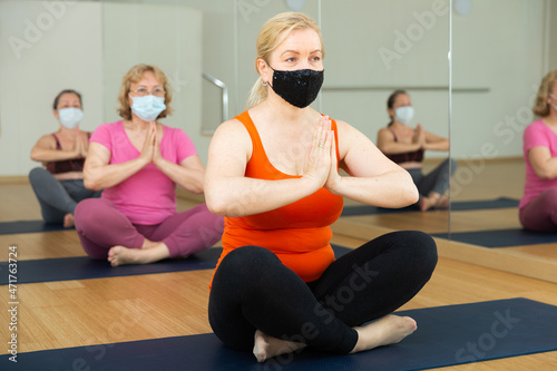 Mature woman in protective mask making yoga meditation in yoga pose - agni stambhasana photo