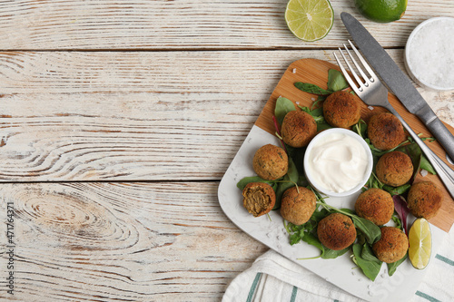 Delicious falafel balls with herbs, lime and sauce on wooden table, flat lay. Space for text