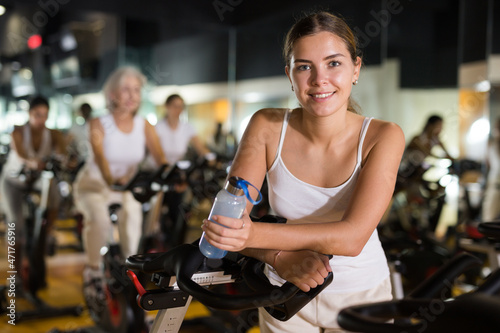 Portrait of young attractive woman who drinking water during cycling class in modern gym