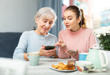 Positive young girl showing pictures on her smartphone to interested elderly mother while sitting at table in cozy dining room.