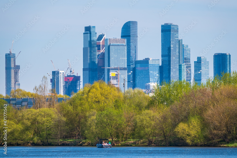 Obraz premium River and green trees on background modern skyscrapers in the Moscow city. Panorama of new Moscow City buildings in spring
