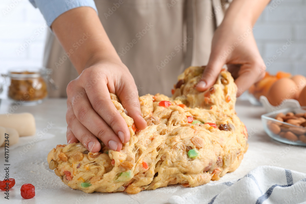 Woman kneading dough with candied fruits and nuts for Stollen at white table, closeup. Baking traditional German Christmas bread Woman kneading dough with candied fruits and nuts for Stollen at white table, closeup. Baking traditional German Christmas bread