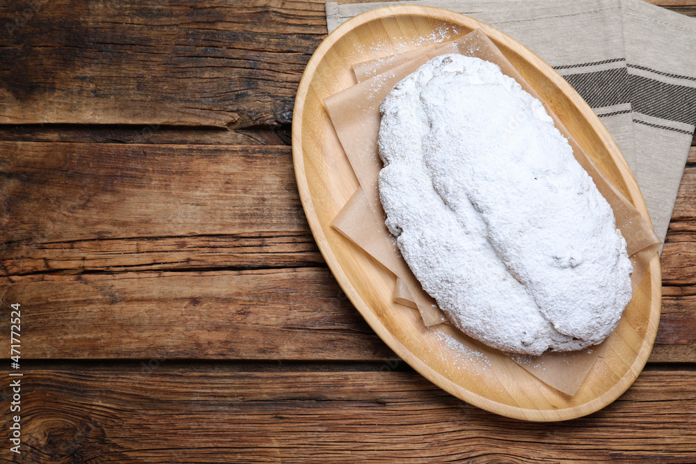 Plate of delicious Stollen sprinkled with powdered sugar on wooden table, top view. Space for text Plate of delicious Stollen sprinkled with powdered sugar on wooden table, top view. Space for text