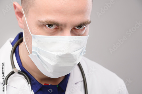 Young caucasian angry doctor in mask and robe looks ominously into the camera. Vaccination conspiracy photo