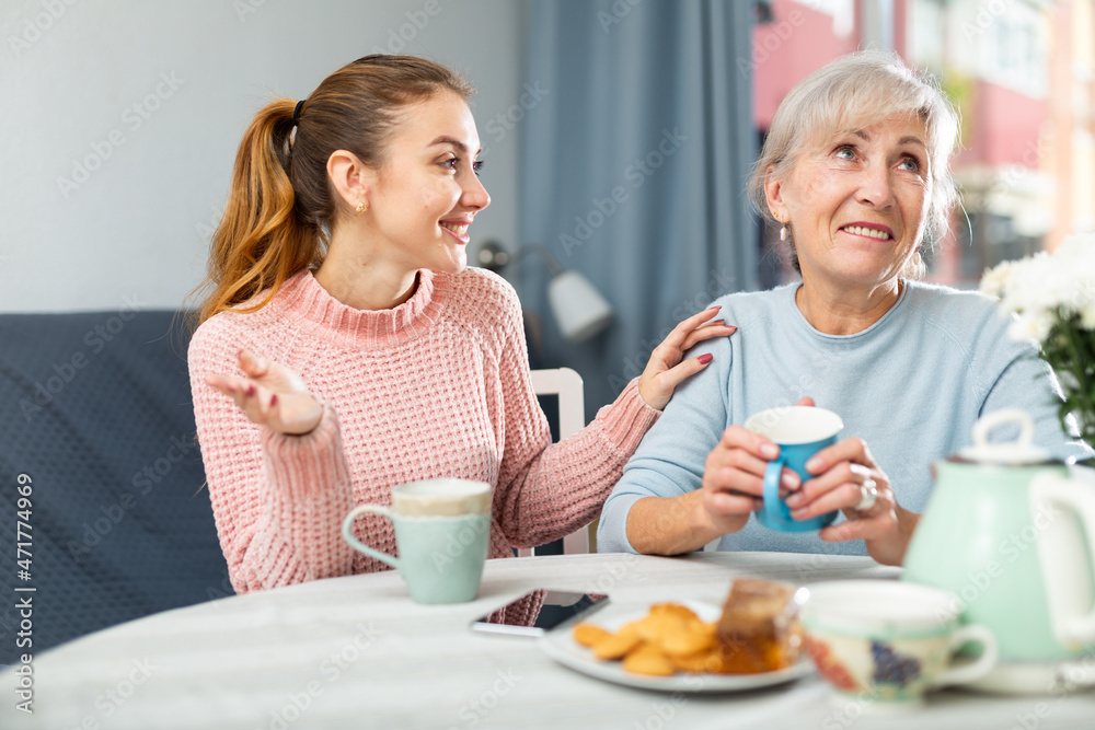 Senior woman talking with her granddaughter while they're drinking coffee in kitchen.