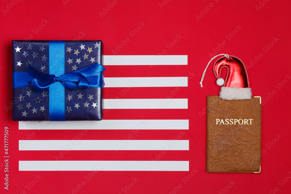 Fototapeta premium American flag composition with blue gift decorated with glittering stars and passport on red background. Merry christmas and happy new year concept..Space for text.