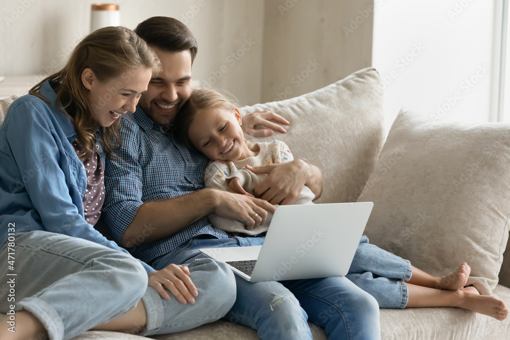 Happy affectionate bonding young couple parents cuddling little smiling child daughter, watching funny family comedian movie or favorite cartoons online on computer, having fun at home, tech addiction Happy affectionate bonding young couple parents cuddling little smiling child daughter, watching funny family comedian movie or favorite cartoons online on computer, having fun at home, tech addiction