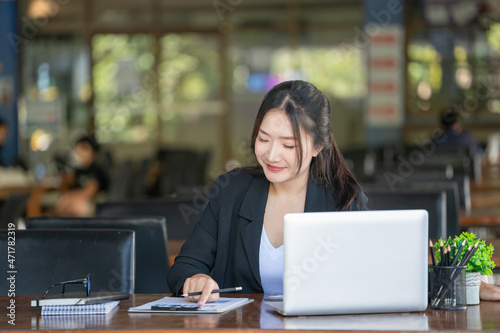 Asian young businesswomen use laptops sitting at a wooden table of a modern coffee shop.