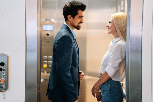 Valokuva Handsome young man and beautiful woman looking at each other smiling standing inside of elevator in shopping mall