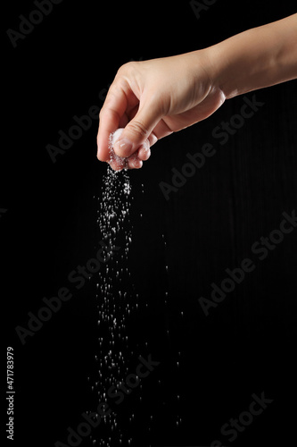 Hand sprinkling sugar on black background