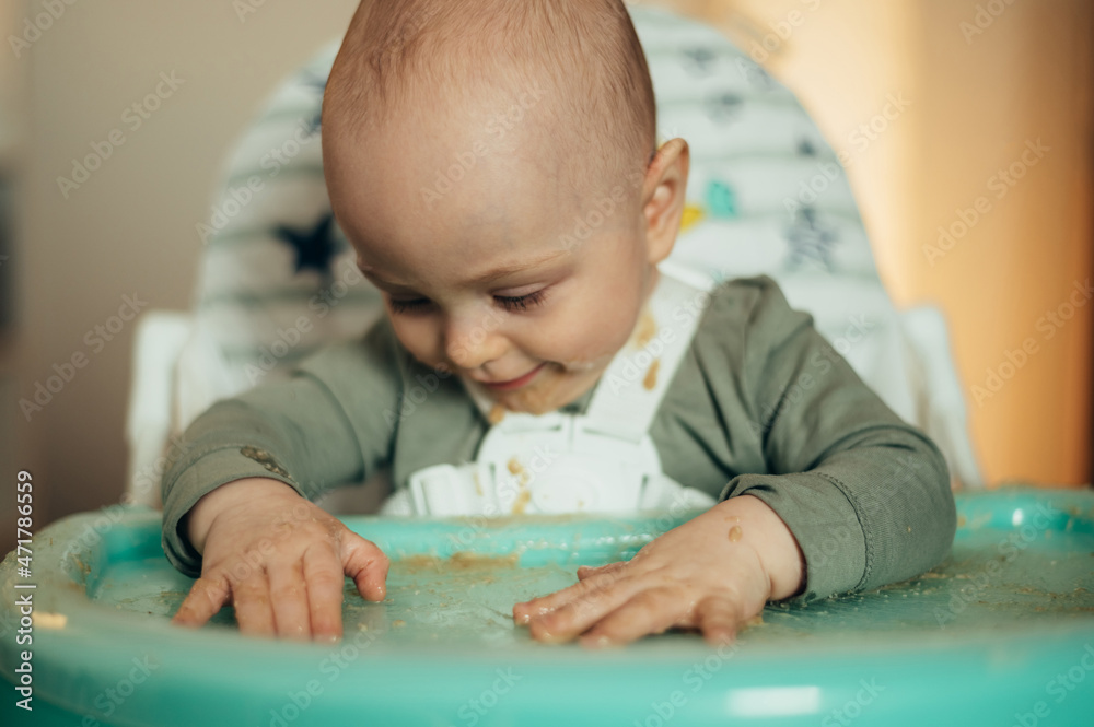 Baby eating with a face stained in food while in a child's dining chair Baby eating with a face stained in food while in a child's dining chair