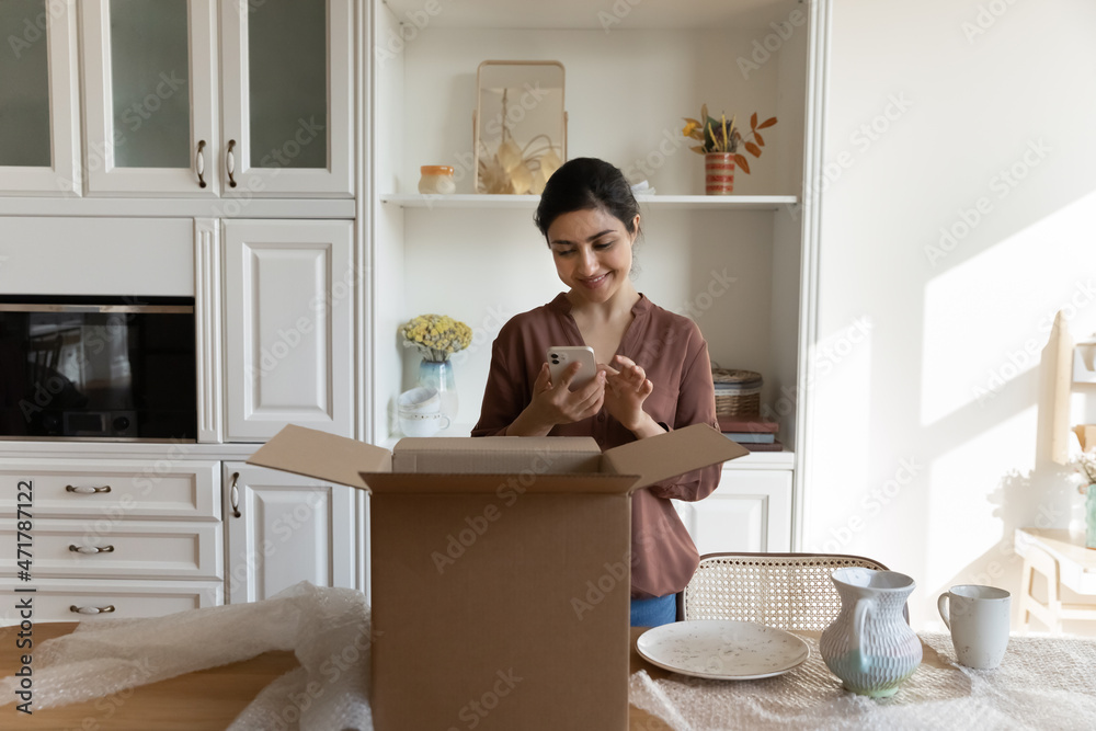 Φωτογραφία Happy millennial indian woman holding cellphone, leaving positive review feeling excited of purchasing high quality dinnerware set in internet store, satisfied with fast fragile delivery service