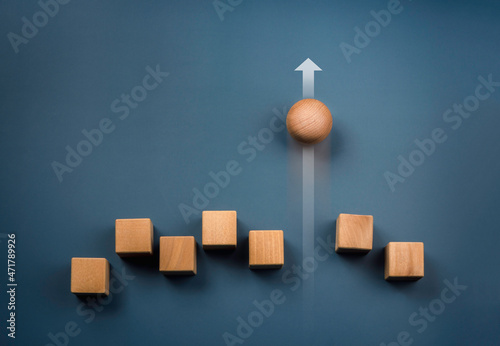 Leadership, business success, unique, difference, challenge, and motivation concepts. Wooden sphere rolling faster leading with rising arrow and following with wood cube blocks on blue background.