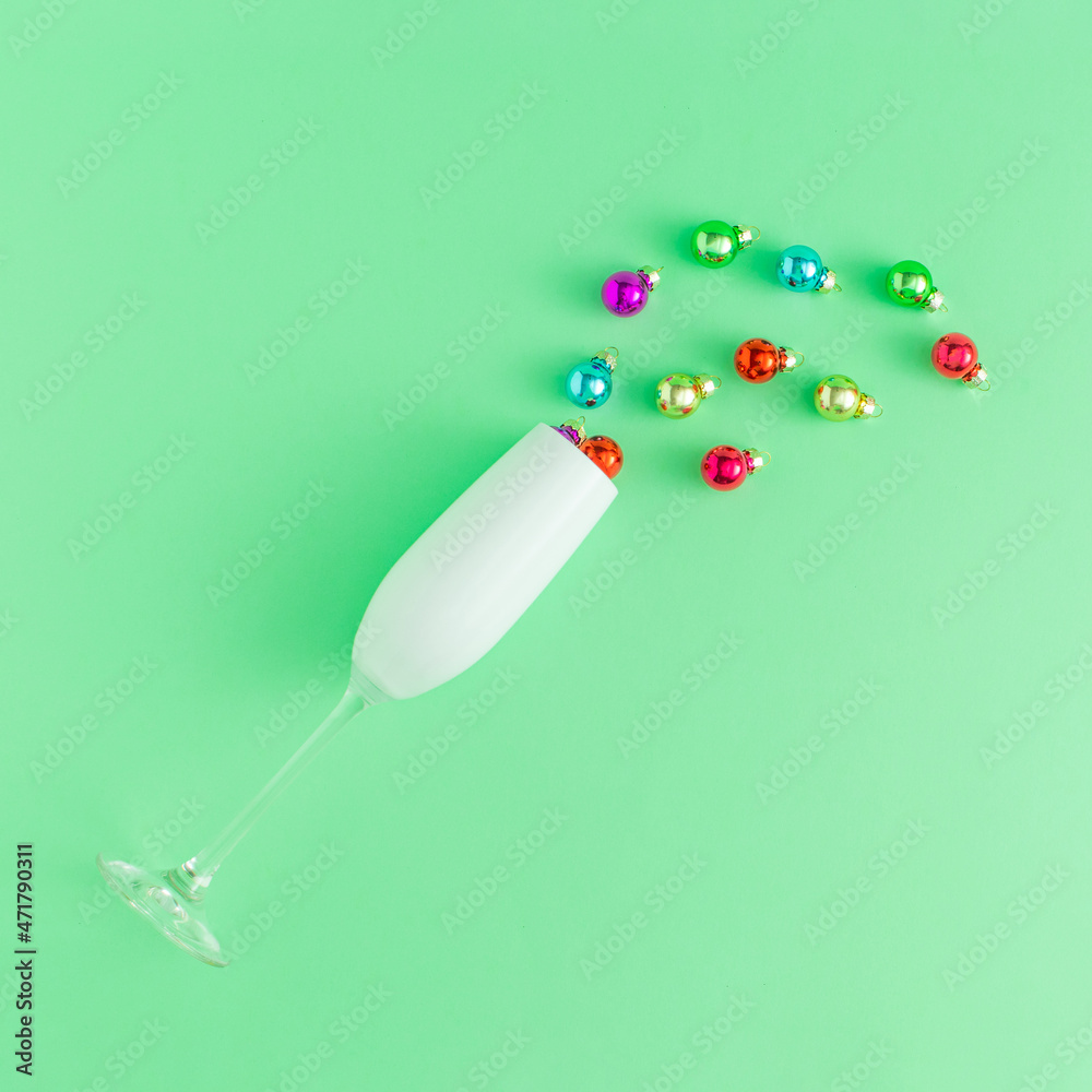 Champagne glass with colorful Christmas baubles against light green background, Minimal New Year party concept. Creative holiday idea. Champagne glass with colorful Christmas baubles against light green background, Minimal New Year party concept. Creative holiday idea.