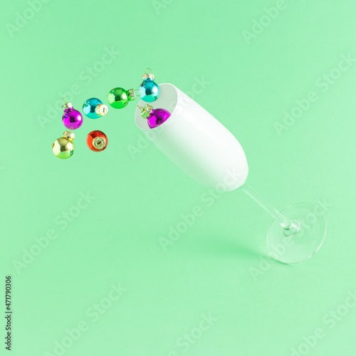 Champagne glass with colorful Christmas baubles against light green background, Minimal New Year party concept. Creative holiday idea.