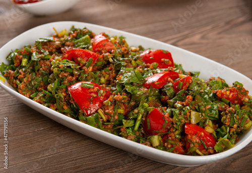 Tabbouleh salad with bulgur, tomatoes, parsley and green onion in plate on wooden table. Traditional middle eastern or arab dish.
