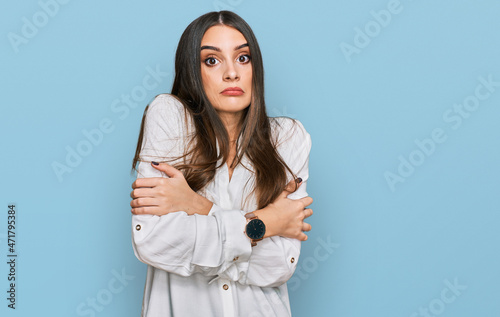 Young beautiful woman wearing casual white shirt shaking and freezing for winter cold with sad and shock expression on face