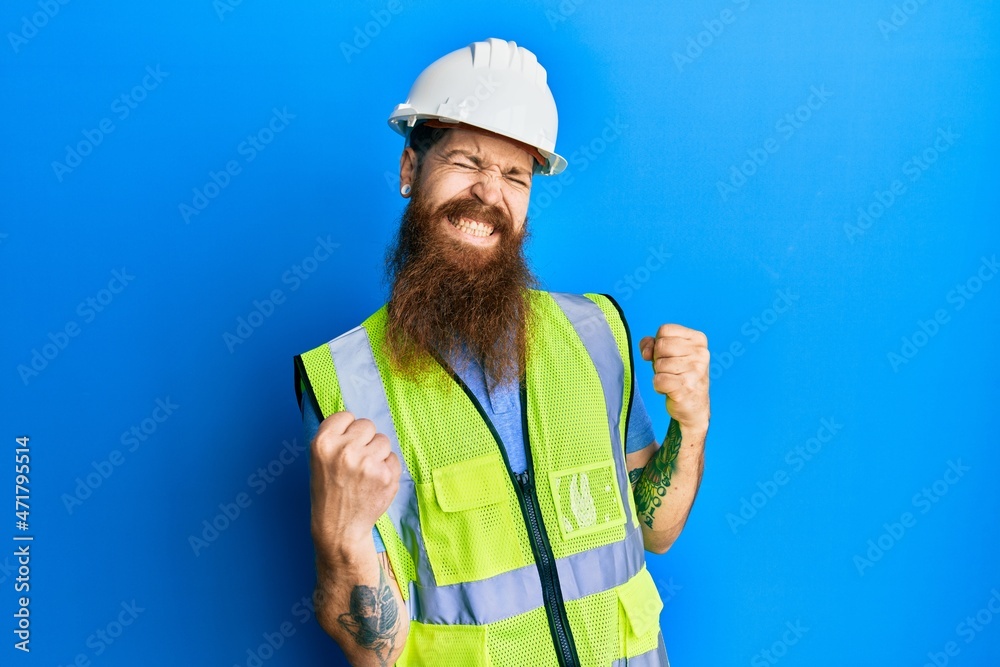 Redhead man with long beard wearing safety helmet and reflective jacket very happy and excited doing winner gesture with arms raised, smiling and screaming for success. celebration concept. Redhead man with long beard wearing safety helmet and reflective jacket very happy and excited doing winner gesture with arms raised, smiling and screaming for success. celebration concept.